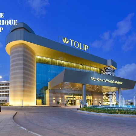 עיין סוחנה Tolip Resort El Galala Majestic מראה חיצוני תמונה The photo shows a modern hotel building named "Tolip Resort & Spa," featuring a sleek architectural design with large glass windows. The hotel is illuminated against a twilight sky, showcasing its prominent signage. In the foreground, there is a well