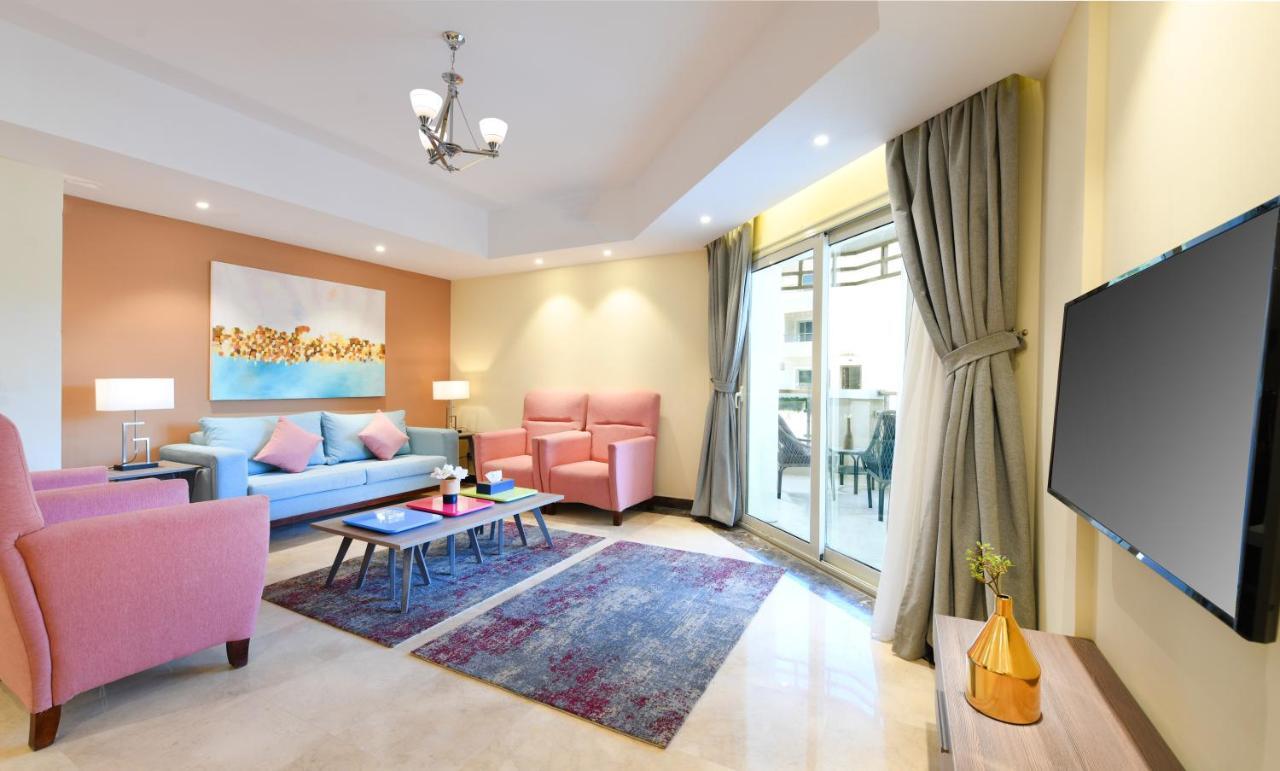 עיין סוחנה Tolip Resort El Galala Majestic חדר תמונה The photo shows a modern living room that features a cozy and stylish design. There is a light blue sofa adorned with pastel pink cushions, accompanied by two pink armchairs. A coffee table sits in front, placed on a colorful area rug that adds warmt