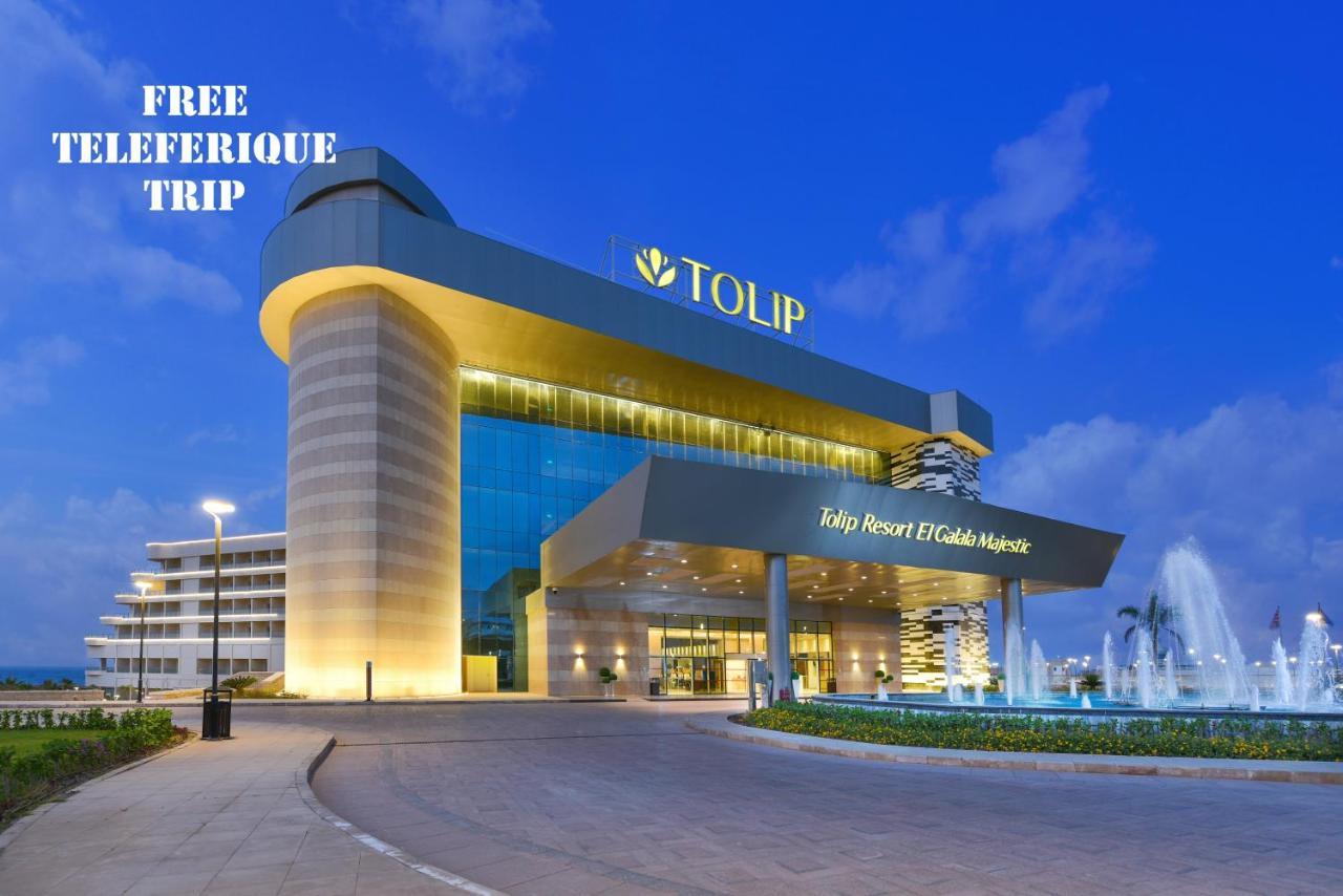 עיין סוחנה Tolip Resort El Galala Majestic מראה חיצוני תמונה The photo shows a modern hotel building named "Tolip Resort & Spa," featuring a sleek architectural design with large glass windows. The hotel is illuminated against a twilight sky, showcasing its prominent signage. In the foreground, there is a well