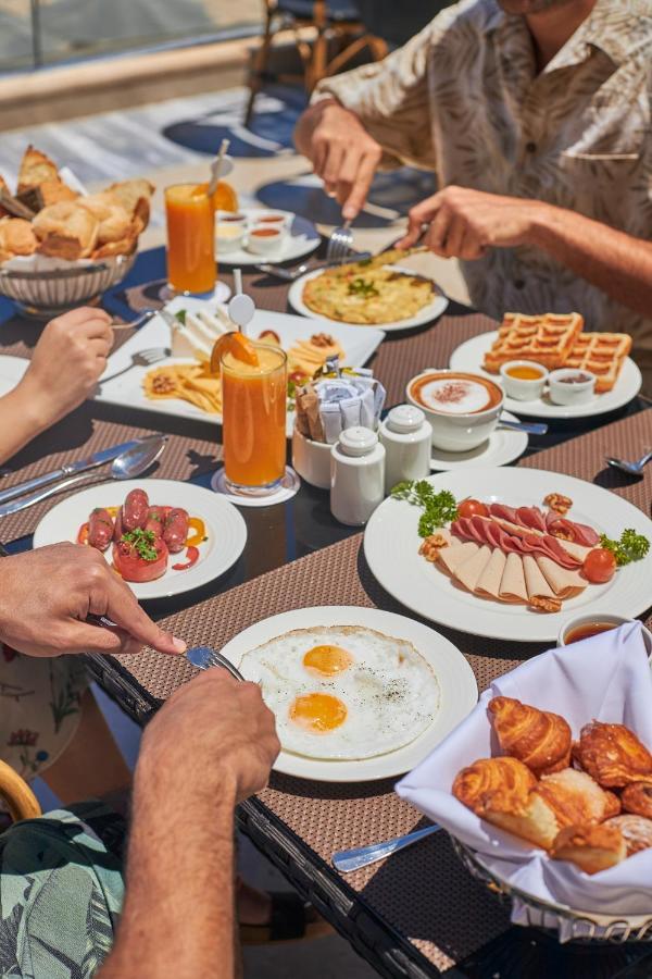 עיין סוחנה Tolip Resort El Galala Majestic מראה חיצוני תמונה The photo features a spread of breakfast dishes on a table. There are two sunny-side-up eggs on one plate, surrounded by various food items, including slices of ham, sausages, and fresh tomatoes. Another plate holds a serving of waffles. A bowl with 