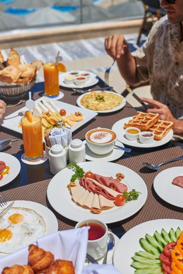 עיין סוחנה Tolip Resort El Galala Majestic מראה חיצוני תמונה The photo shows a breakfast spread laid out on a table. There are several plates with a variety of food items, including:

1. **Sliced Cold Cuts**: A plate featuring various cold meats, accompanied by garnishes like cherry tomatoes and lettuce.
2. **