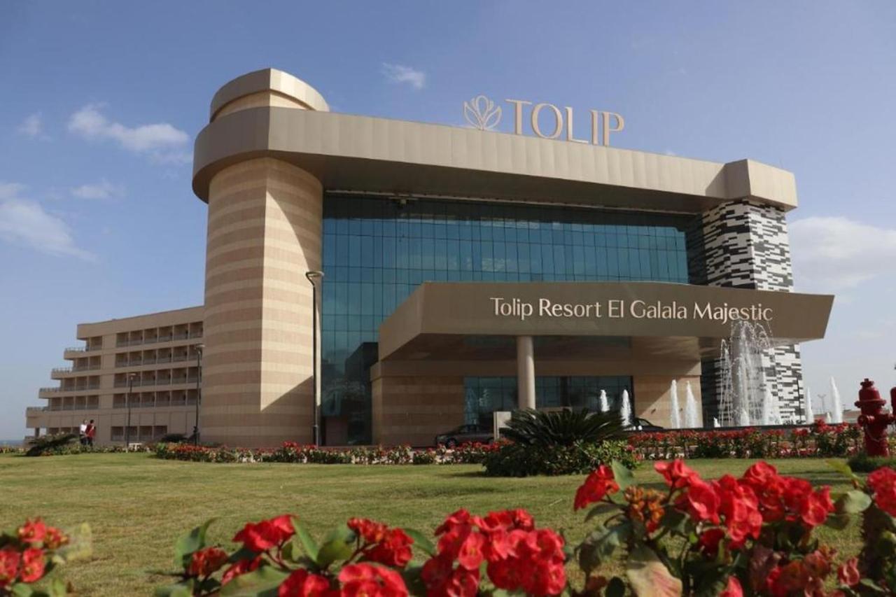 עיין סוחנה Tolip Resort El Galala Majestic מראה חיצוני תמונה The photo shows a modern hotel building named "Tolip Resort El Galala Majestic." The structure features a distinctive architectural design with large glass windows and a prominent entrance. Surrounding the building are well-maintained lawns and vibra