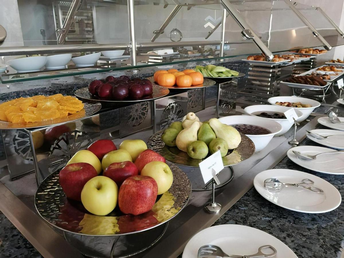 עיין סוחנה Tolip Resort El Galala Majestic מראה חיצוני תמונה The photo displays a buffet setup featuring an assortment of fresh fruits arranged on several tiered trays. There are red and green apples, pears, grapes, and oranges. Adjacent to the fruit display, there are several bowls containing various other fo