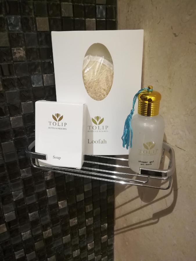 עיין סוחנה Tolip Resort El Galala Majestic מראה חיצוני תמונה The photo shows a small metal shelf containing three items related to personal care. 

1. **Soap**: A white box labeled "TOLIP" with the word "Soap" visible on the front.
2. **Loofah**: A package with the same "TOLIP" branding, containing loofah.
3. 